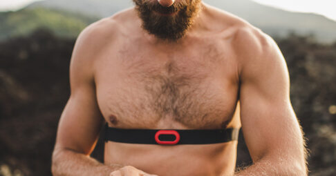 Athletic man watching training results on smart watch or fitness tracker. Running topless and using chest heart rate monitor. Body close-up.