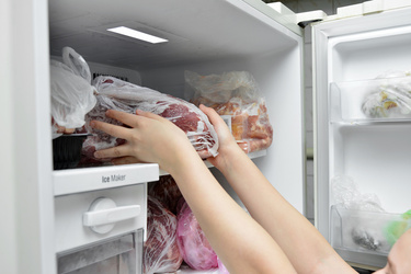 The girl takes out a bag of frozen meat from the freezer in the kitchen at home.